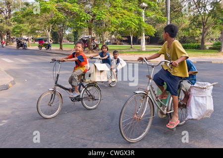 Portrait horizontal d'un groupe de jeunes enfants cambodgiens équitation sur des bicyclettes surdimensionnées en bas de la route. Banque D'Images