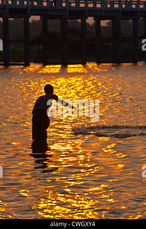 Un pêcheur jette son filet ci-dessous U BEINS Pont sur le lac Taungthaman au lever du soleil - AMARAPURA, MYANMAR Banque D'Images