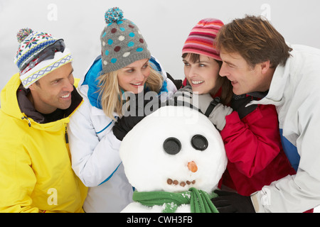 Groupe d'amis Building Snowman sur vacances de neige en montagne Banque D'Images