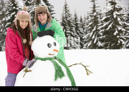 Deux adolescents Building Snowman sur vacances de neige en montagne Banque D'Images