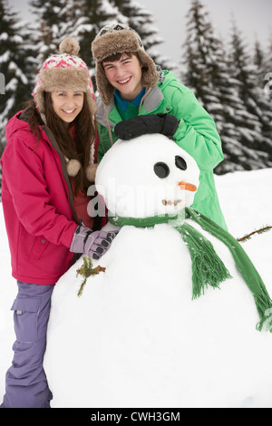 Deux adolescents Building Snowman sur vacances de neige en montagne Banque D'Images