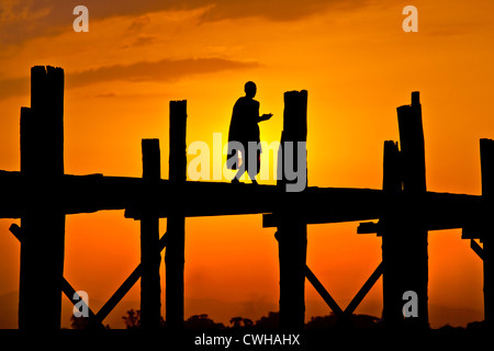 Le moine birman utilise le pont en teck U BEINS de commuer à travers le lac Taungthaman au lever du soleil - AMARAPURA, MYANMAR Banque D'Images