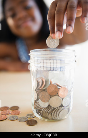 Black girl putting coins dans un pot Banque D'Images