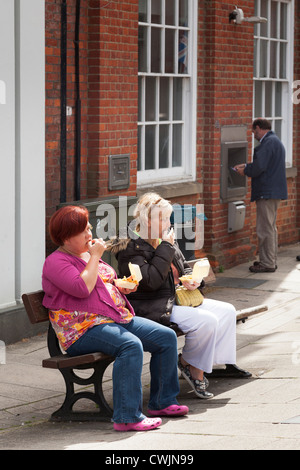 Deux femmes s'assit sur le banc en Romsey eating fast food Banque D'Images