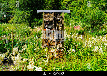 Un cadre en bois insect house construit de paille, briques, bois, écorce et le carton situé dans un jardin naturel plein de fleurs sauvages Banque D'Images