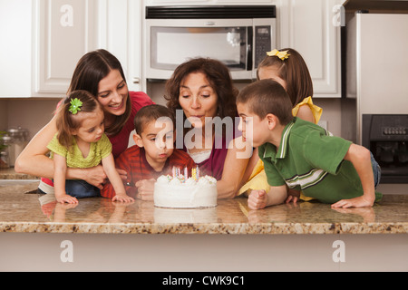 La famille de race blanche dans la cuisine qui sort du gâteau d'anniversaire Banque D'Images