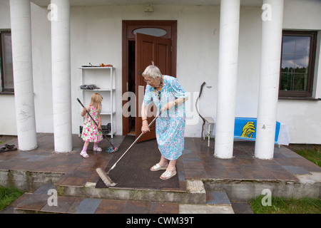 Grand-mère polonaise et le balayage et le nettoyage à l'arrière petite-fille d'entrée porche façon dont l'âge 86 et 4. Zawady Centre de la Pologne Banque D'Images