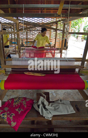 Close up vertical d'une femme tissant les fils de soie rouge sur le tissu sur un métier à une usine de fabrication de la soie au Cambodge. Banque D'Images