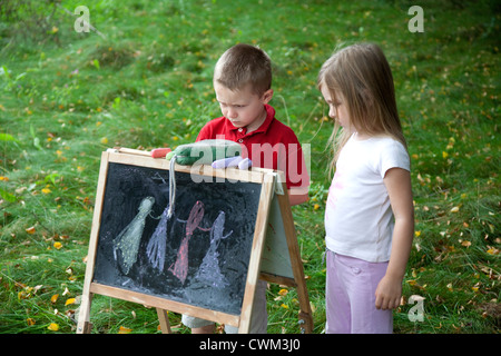 Jeune garçon et fille dessin sur tableau dans l'air extérieur champ age 6 et 8. Zawady Centre de la Pologne Banque D'Images