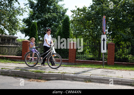 Maman polonaise son vélo à pied vers le bas avec trottoir daughter eating ice cream cone équitation derrière. La Pologne centrale Rzeczyca Banque D'Images