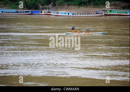 Quatre moines bouddhistes de parapluies dans un canot sur la rivière Nam Khan à Luang Prabang, Laos. Banque D'Images