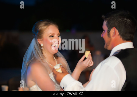 Bride and Groom macule chaque autres faces avec du glaçage pendant un gâteau symbolique traditionnelle américaine à leur mariage. Banque D'Images