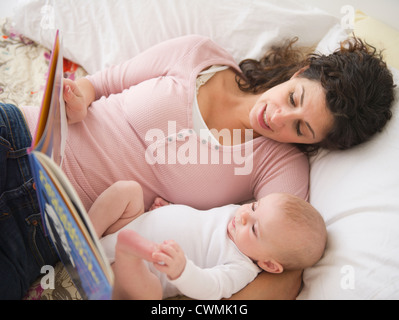 USA, New Jersey, Jersey City, Mère et baby boy (2-5 months) lying together on bed, reading book Banque D'Images
