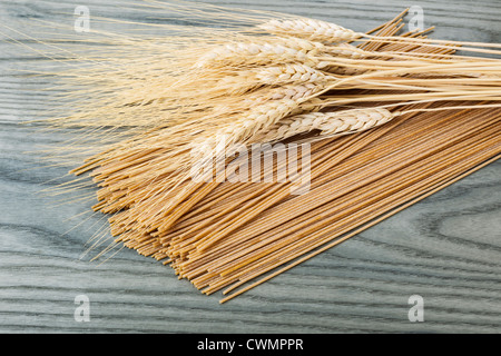 Spaghetti de blé entier brut avec des grains de blé sur le dessus avec le bois de frêne blanc en arrière-plan Banque D'Images