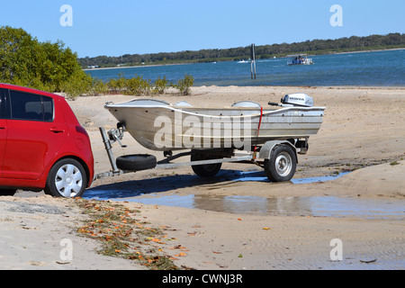 La Suzuki Swift rouge remorque bateau dans l'eau en face de la plage Banque D'Images