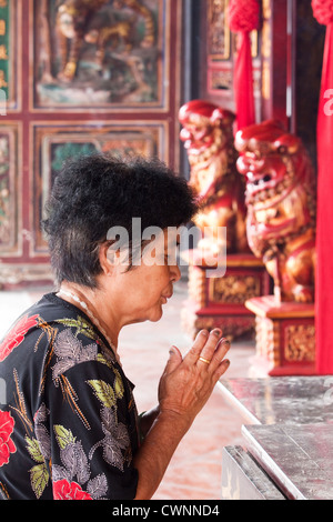 Vieille femme chinoise de Malaisie offrant des prières dans un temple bouddhiste avec les mains jointes, les yeux fermés et la tenue de fumeurs d'encens dans la ville de Malacca Banque D'Images