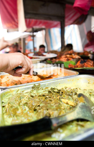 Selective focus sur une main prenant en self service à un street food vente d'aliments de rue de Malaisie. Un buffet de plats colorés conteneurs Banque D'Images