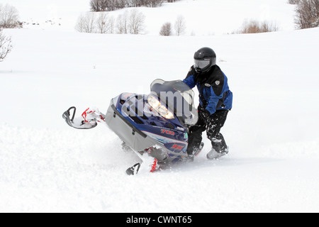 Cavalier motoneige s'amusant et en tournant dans la neige fraîche et blanche. Les virages serrés dans une prairie de montagne de haute altitude. Banque D'Images