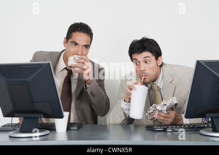 Hommes d'eating fast food at desk in office Banque D'Images