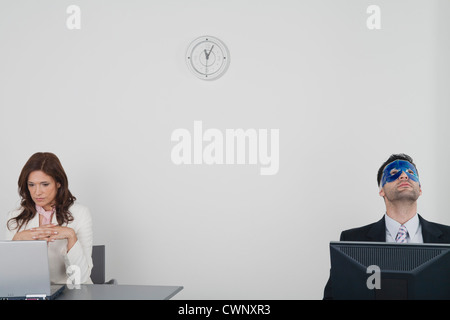 Businesswoman working with laptop computer, businessman relaxing with eye mask Banque D'Images