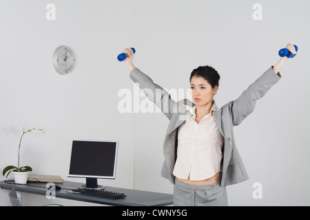 Young businesswoman exerçant dans office with dumbbells Banque D'Images