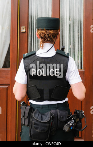 Police woman attend devant la porte d'une maison Banque D'Images