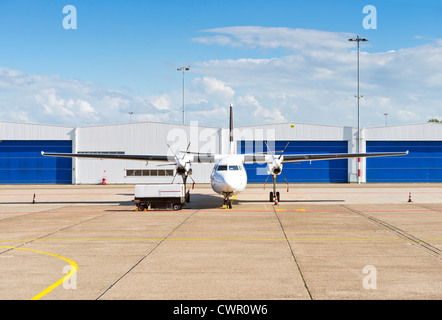 Avions à hélice et chariot en face de hangars sur la piste d'un petit aéroport Banque D'Images