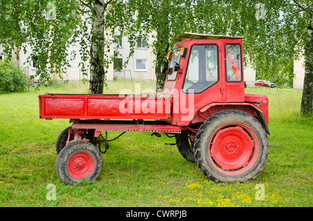 Tracteur agricole rouge rétro avec remorque près de Birch Tree dans la petite ville. Banque D'Images