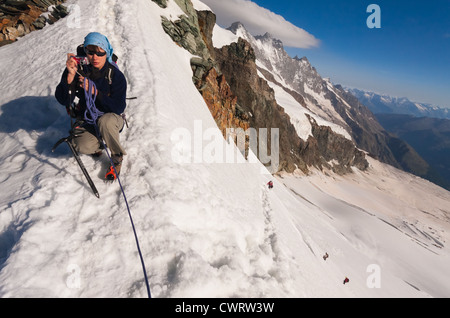 Un grimpeur saisit l'occasion de prendre une photographie sur Feechopf ridge que quatre autres grimpeurs de l'approche ci-dessous. Banque D'Images