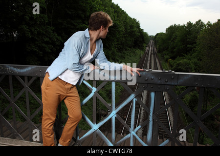 Jeune homme sérieux debout sur pont de chemin de fer Banque D'Images