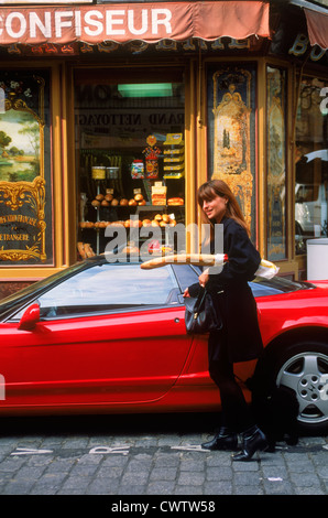 Femme à Paris baguette boulangerie laissant entrer dans cher voiture sport rouge avec caniche français sur cobblestone street Banque D'Images