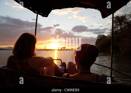 Deux femmes regardant un coucher de soleil africain sur le lac Manze dans un bateau, Selous, Tanzanie Afrique Banque D'Images