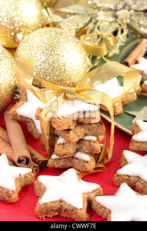 Star-shaped Christmas cookies à la cannelle sur un fond rouge. Décoré avec des décorations de Noël et des bâtons de cannelle. Banque D'Images