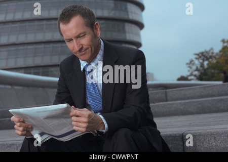 Businessman reading newspaper on steps Banque D'Images