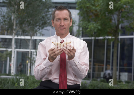 Businessman eating sandwich dans city park Banque D'Images