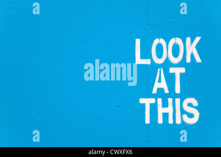 Au pochoir blanc graffiti sur un mur peint en bleu avec les mots : Regardez ce Banque D'Images