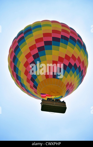 Ballon à air chaud à damiers colorés avec grand panier vu du dessous contre ciel bleu clair Banque D'Images