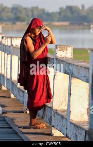 Le Myanmar, Birmanie, Mandalay. Le moine bouddhiste en tenant Cell Phone Photo sur le pont U Bein, Amarapura. Banque D'Images