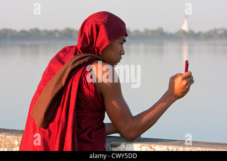 Le Myanmar, Birmanie, Mandalay. Le moine bouddhiste en tenant Cell Phone Photo sur le pont U Bein, Amarapura. Banque D'Images