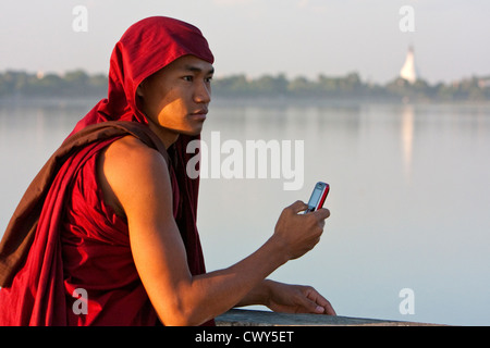 Le Myanmar, Birmanie, Mandalay. Le moine bouddhiste en tenant Cell Phone Photo sur le pont U Bein, Amarapura. Banque D'Images