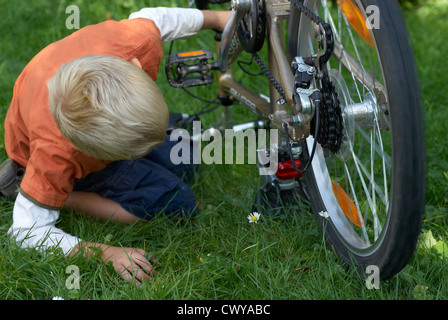 Enfant garçon blond d'examiner et de fixer son vélo à l'extérieur de l'été Banque D'Images