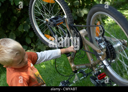 Enfant garçon blond d'examiner et de fixer son vélo à l'extérieur de l'été Banque D'Images