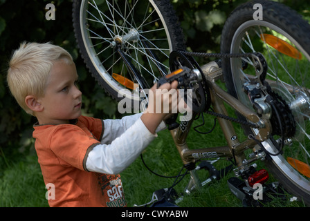 Enfant garçon blond d'examiner et de fixer son vélo à l'extérieur de l'été Banque D'Images