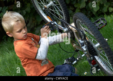 Enfant garçon blond d'examiner et de fixer son vélo à l'extérieur de l'été Banque D'Images