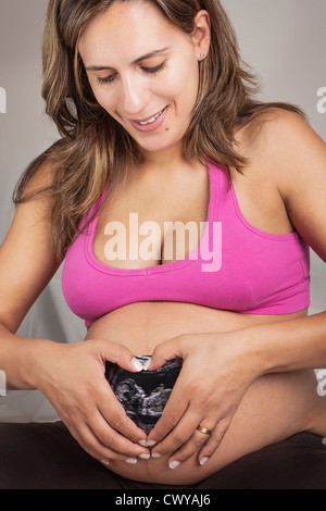 Happy pregnant woman Making un Cœur avec ses mains sur le résultat de l'examen échographique Banque D'Images