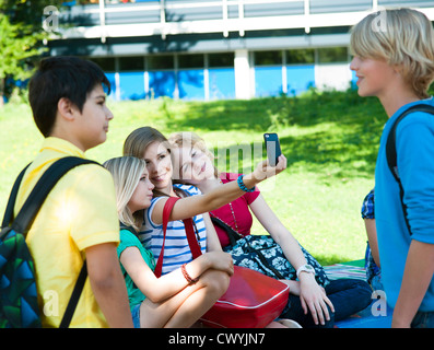 Les filles sur un banc de travail avec téléphone portable et deux garçons regardaient Banque D'Images