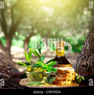 Photo de la vie toujours d'olive, huile d'olive dans la bouteille et l'olive verte dans un bol en verre avec du pain sur le bac à l'extérieur, dans le jardin de fruits frais Banque D'Images