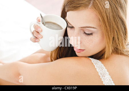Jeune femme avec tasse au lit Banque D'Images