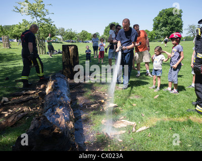 Les pompiers ou les pompiers éteindre un feu dans un tronc d'arbre à Richmond Park et montrer les enfants regarder comment c'est fait Banque D'Images