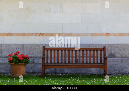 Un banc en face d'un mur à côté de fleurs Banque D'Images
